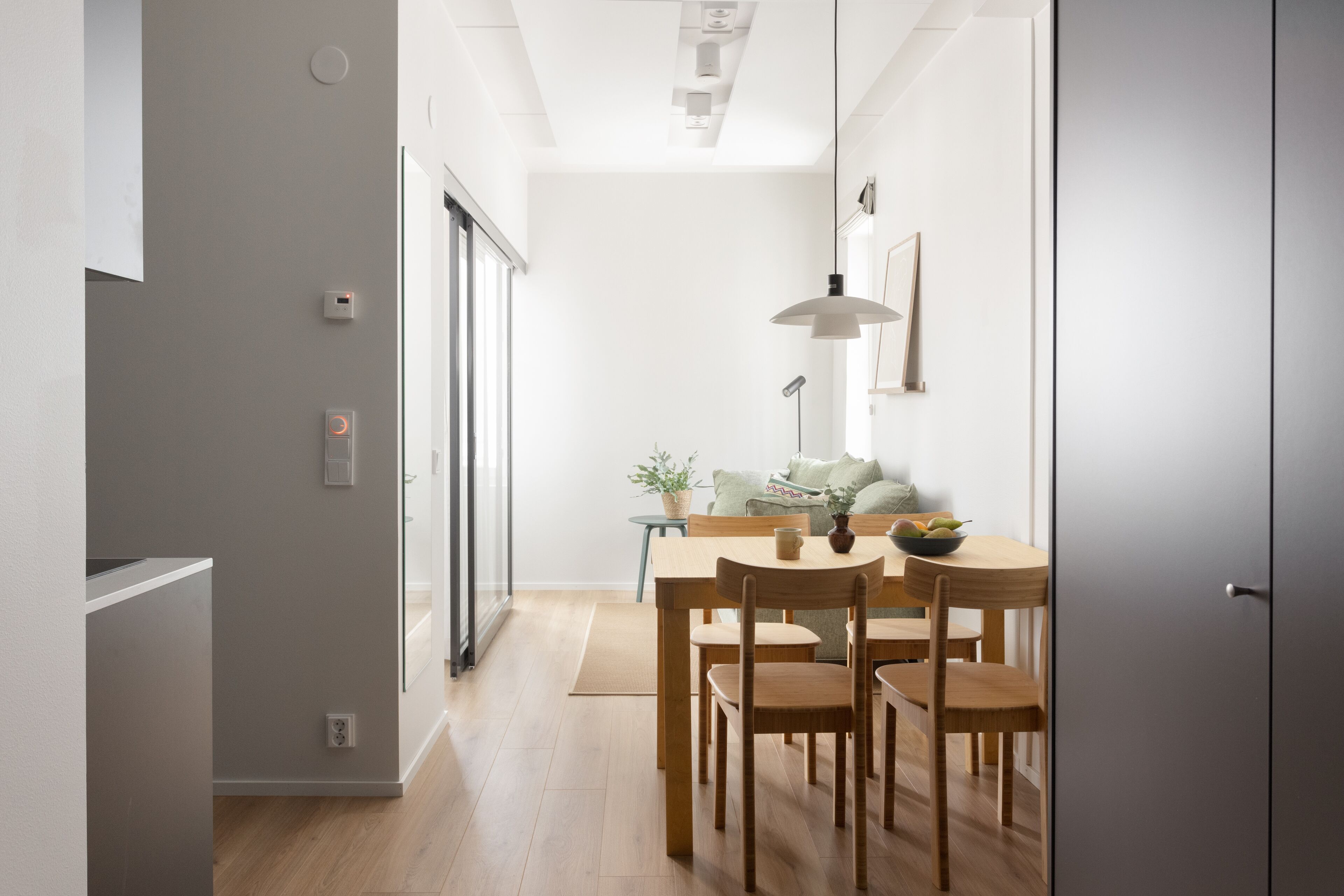 A modern dining area with a wooden table and chairs, a pendant light, and a view into the adjacent room.