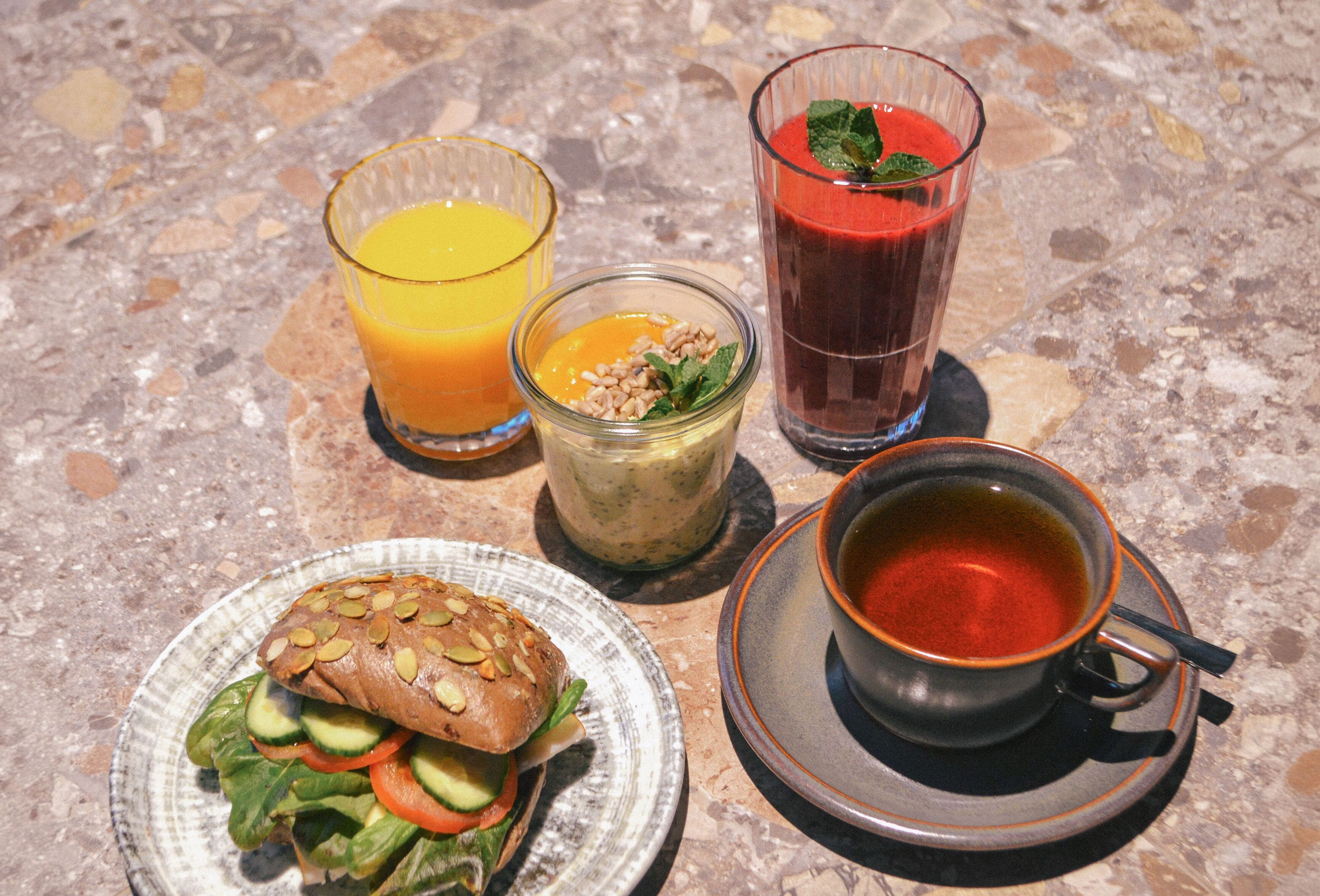 A meal consisting of a sandwich, a glass of orange juice, a glass of red juice, a bowl of soup, and a cup of tea.