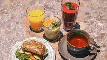 A meal consisting of a sandwich, a glass of orange juice, a glass of red juice, a bowl of soup, and a cup of tea.