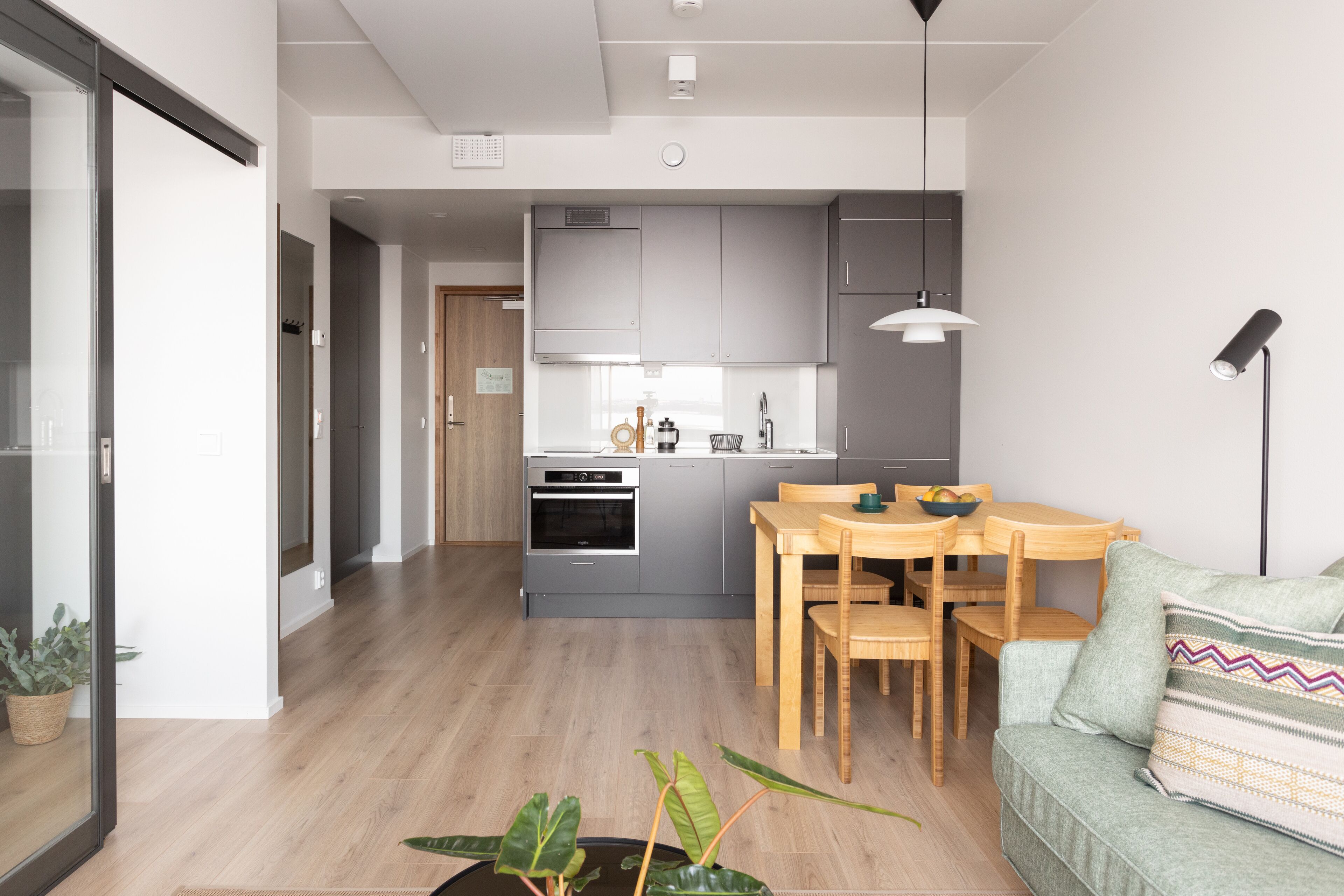 A modern kitchen with grey cabinets, a wooden dining table, and a built-in oven.