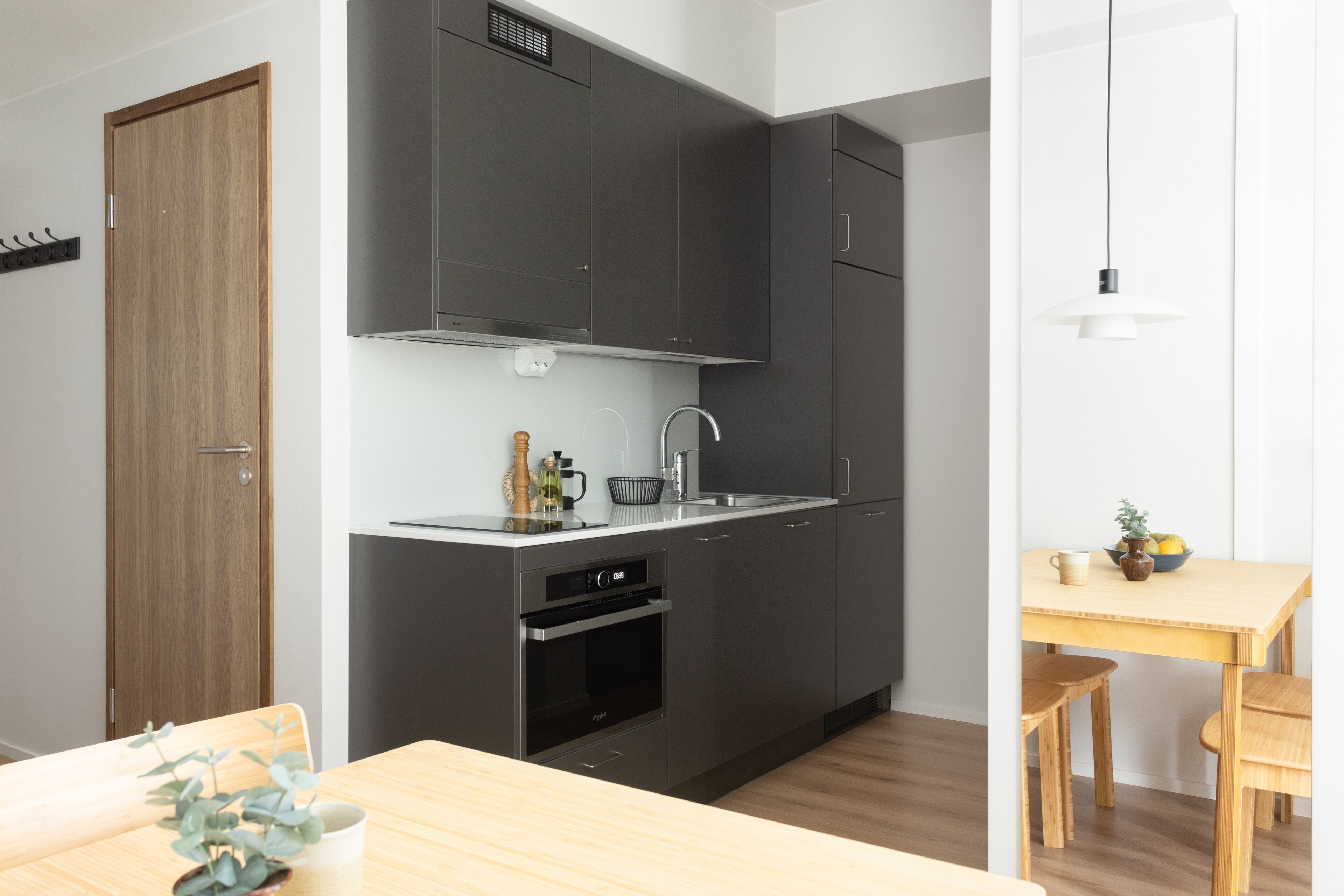 A modern kitchen with dark cabinets, a built-in oven, and a dining area with a wooden table and chairs.