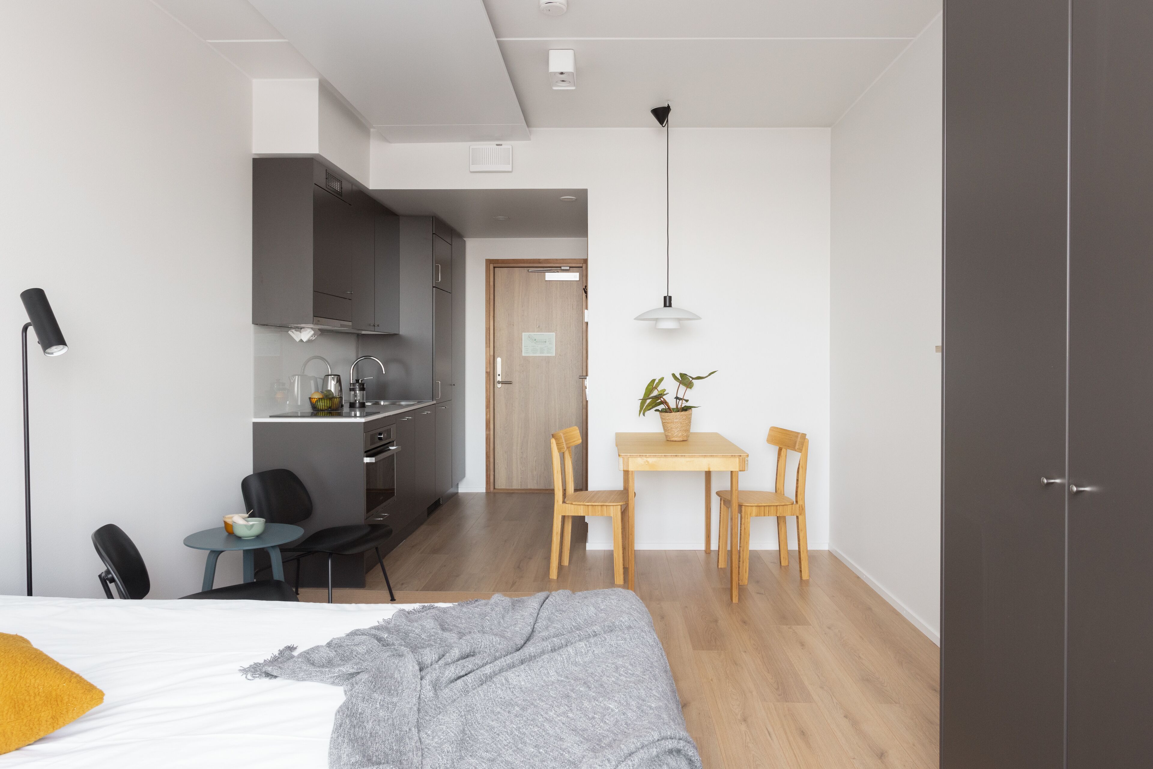Une chambre d’hôtel moderne équipée d’un lit, d’une table de chevet, d’une lampe et d’une petite kitchenette.