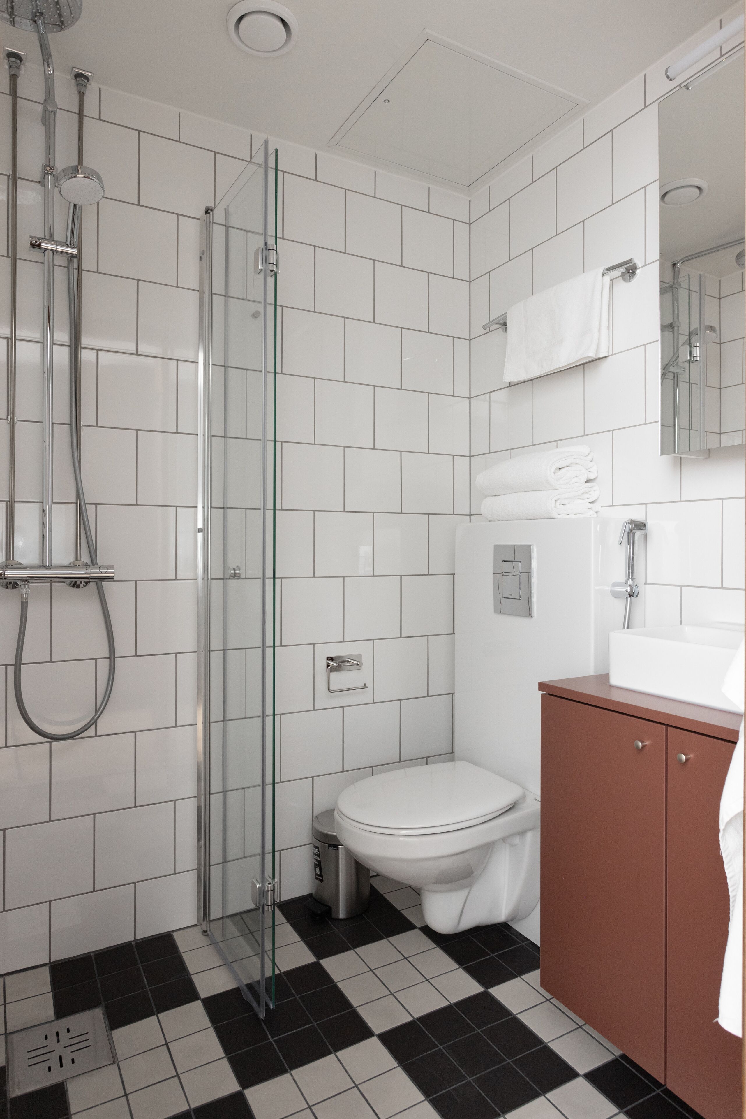 Une salle de bain moderne avec une douche à parois de verre, des toilettes blanches et un meuble-lavabo marron agrémenté d’un miroir.