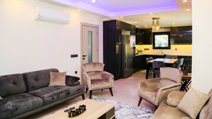 A modern living room with a sofa, armchairs, and a coffee table. A kitchen area with a dining table and chairs is visible in the background. - BEAUTIFUL 4 BEDROOM VILLA WITH PRIVATE POOL&GARDEN IN HEART OF DALYAN MARAS AREA (Dalyan)