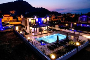 Una villa moderna con piscina, mobiliario exterior y vistas a las colinas circundantes.
