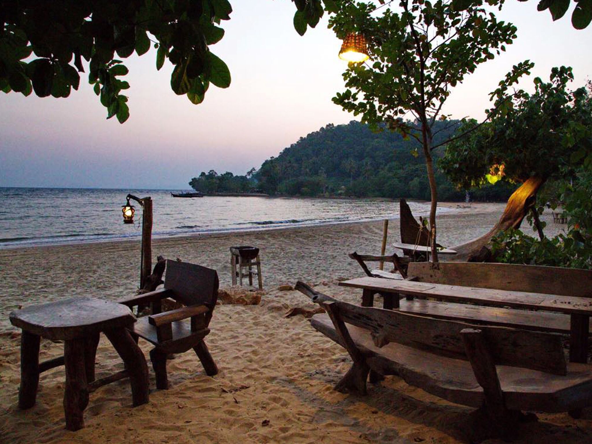 A beach with wooden benches and tables, a lantern, and a boat.