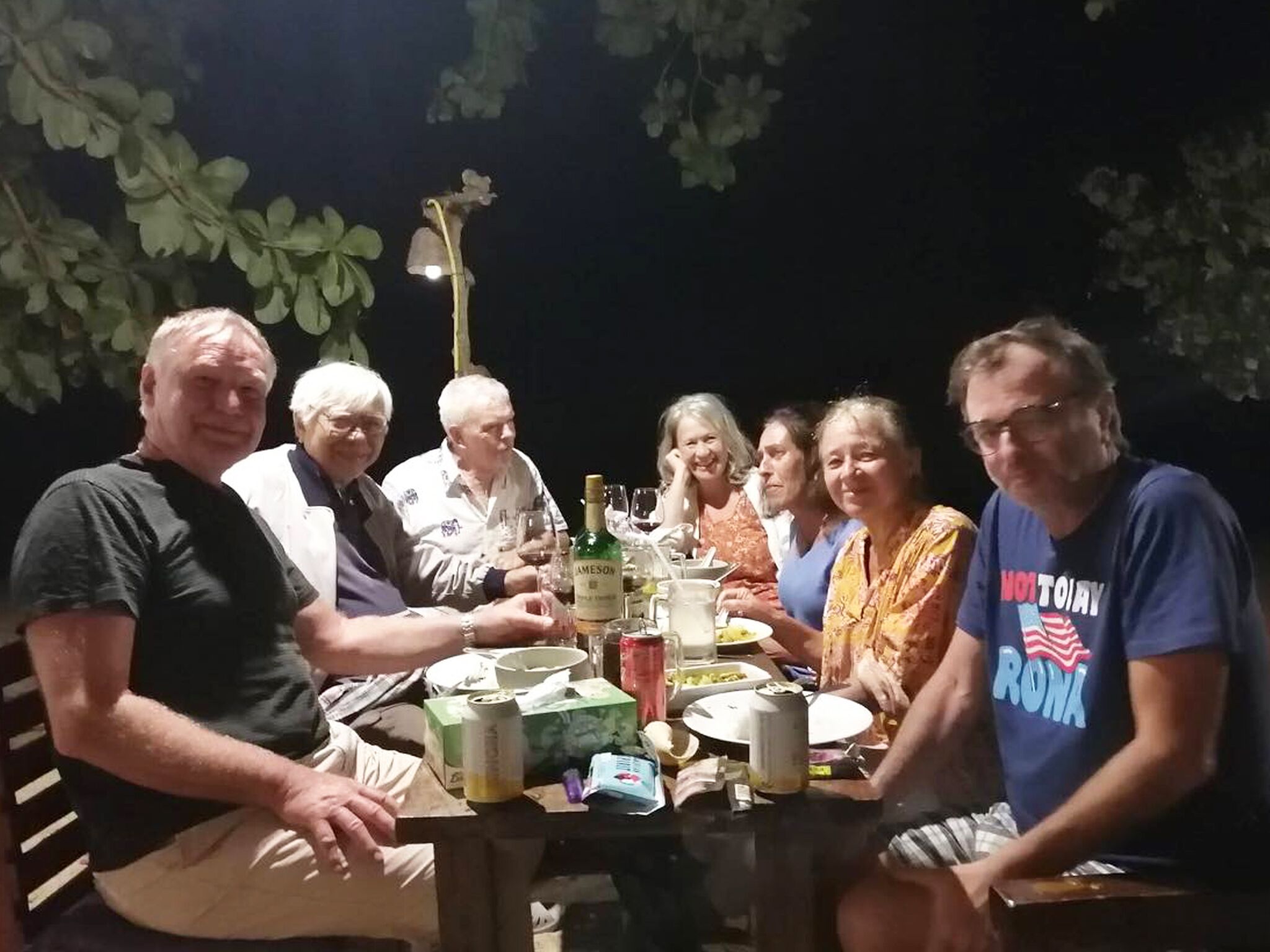 Un grupo de personas sentadas alrededor de una mesa con varios objetos, incluyendo una botella, vasos y platos.