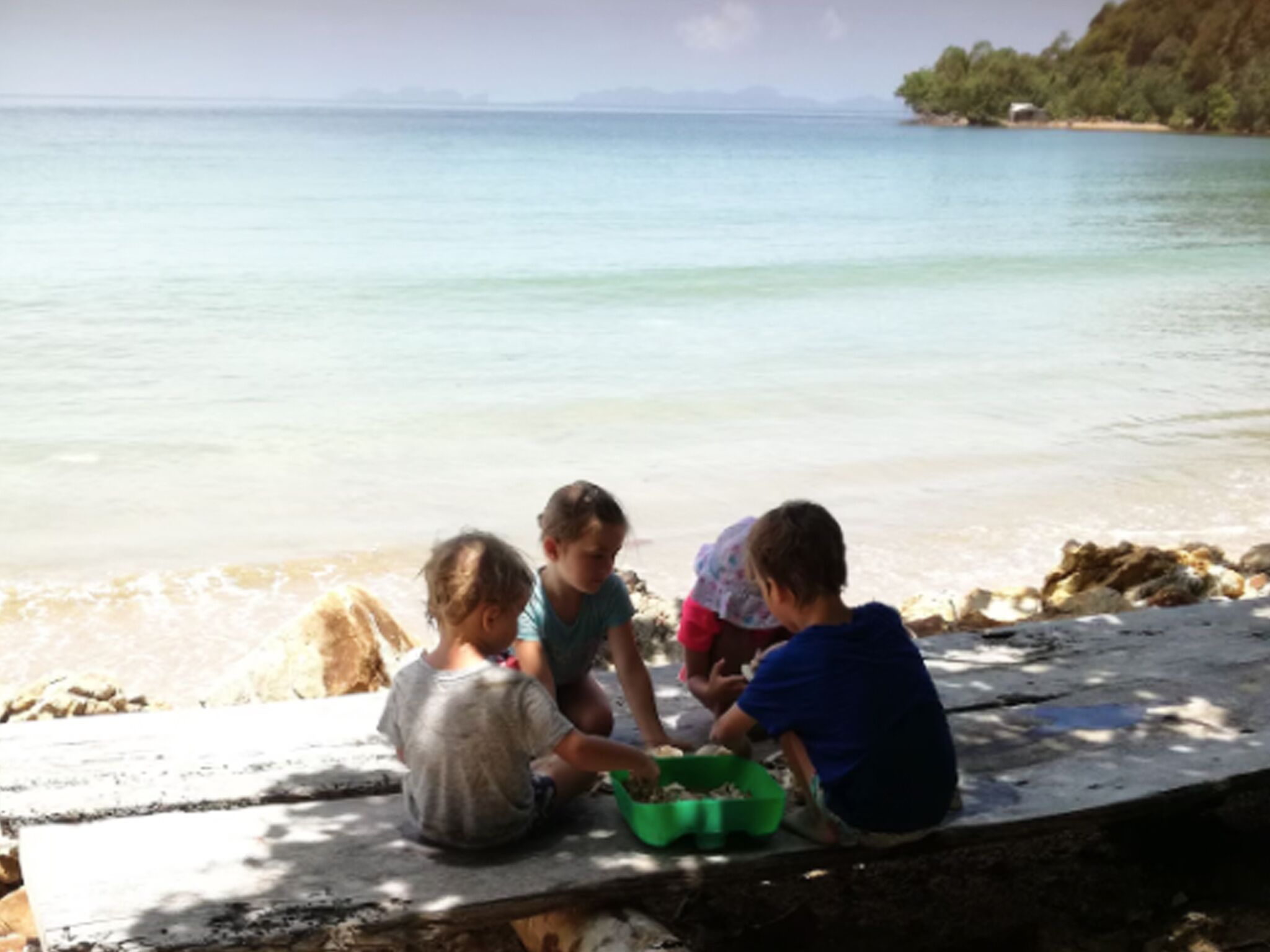 Tre bambini che giocano vicino a una spiaggia con un mare calmo e un litorale roccioso.