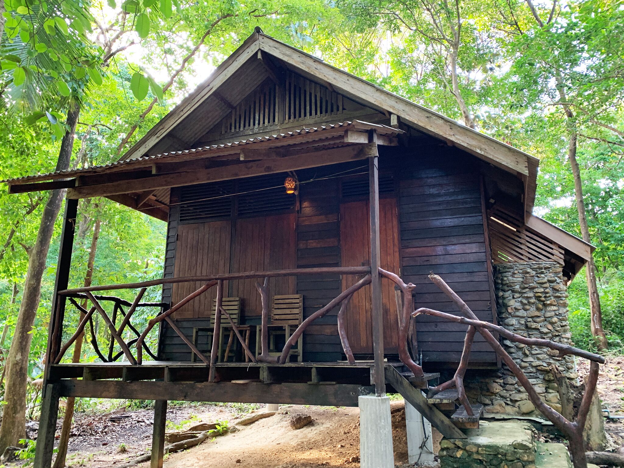 A rustic wooden cabin with a stone foundation, a wooden porch, and a metal railing.