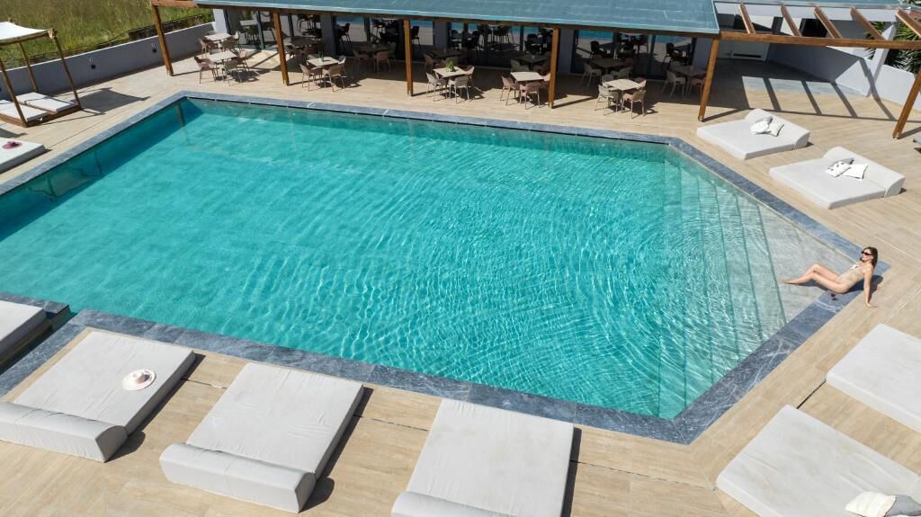 Una piscina rectangular con agua cristalina, rodeada de sillas de descanso y mesas.