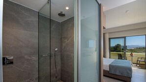 A modern bathroom with a glass shower enclosure, a toilet with a towel, and a balcony with a bed and a table. - Mare Garden (Apokoronas)