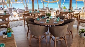 A beachside restaurant with round tables, wicker chairs, and potted plants. - Villa 15 - VIP - Privacy - Blue Bay Beach Villa (Sint Michiel)