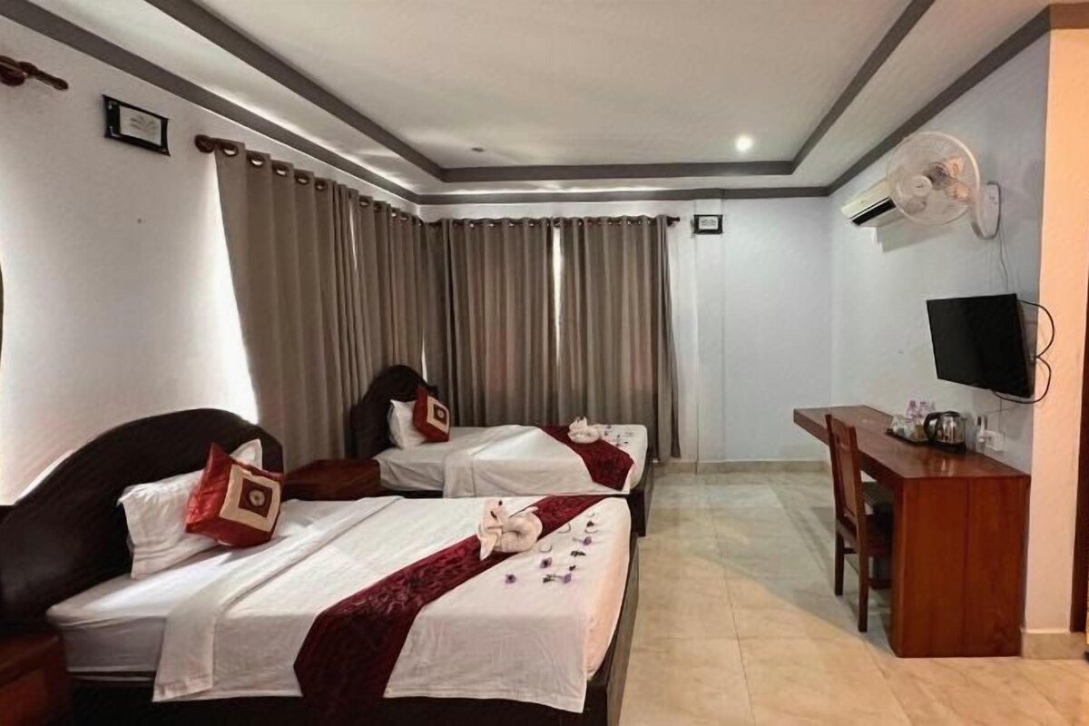A hotel room with two beds, a desk, a TV, and a bathroom.