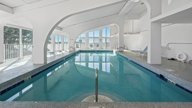 Ein Schwimmbecken mit klarem, blauem Wasser, umgeben von weißen Wänden und großen Fenstern.