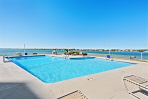 A rectangular swimming pool with a clear blue water, surrounded by lounge chairs and a small table. - Compass Point 108 (Gulf Shores)