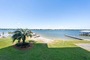A lakeside view with a dock, a beach area, and a palm tree. - Compass Point 108 (Gulf Shores)