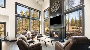 Una sala moderna con chimenea, sofás de cuero y grandes ventanales que dan a una vista del bosque.