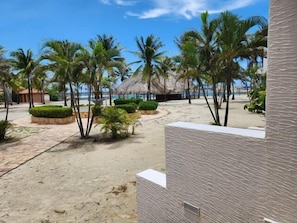 A beachside resort with palm trees, a thatched-roof structure, and a sandy walkway.