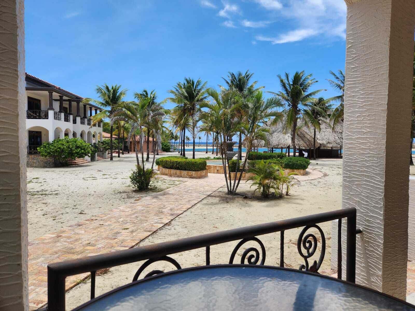 A beachfront courtyard with palm trees, a pool, and a building with balconies.