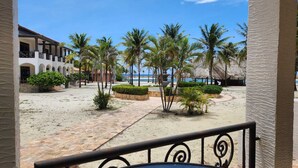 Un cortile affacciato sulla spiaggia, con palme, una piscina e un edificio con balconi.