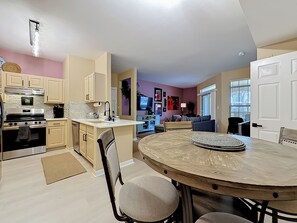 A modern kitchen with a dining area, featuring a central island, built-in appliances, and a seating area with a sofa and TV. - Clearwater Resort-Like Gulf Coast Beach Oasis (Clearwater)