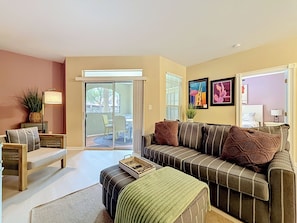 A living room with a sofa, a coffee table, a lamp, and a sliding glass door leading to an outdoor area. - Clearwater Resort-Like Gulf Coast Beach Oasis (Clearwater)
