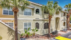 A multi-story residential building with a beige exterior, multiple windows, and palm trees.