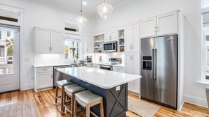 A modern kitchen with white cabinetry, stainless steel appliances, and a large island with bar stools. - BVR 43 - Off The Hook by Liquid Life (Orange Beach)