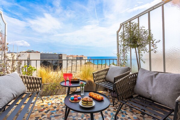 A terrace with wicker furniture, a tiled floor, and a table with food and drinks.