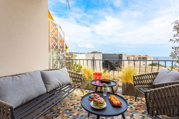 A terrace with a sofa, two tables, and a view of the sea.