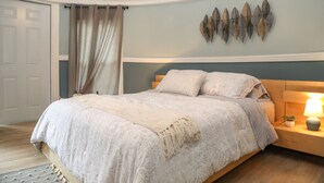 Un dormitorio con cama, mesita de noche con lámpara, una obra de arte en la pared y una puerta.