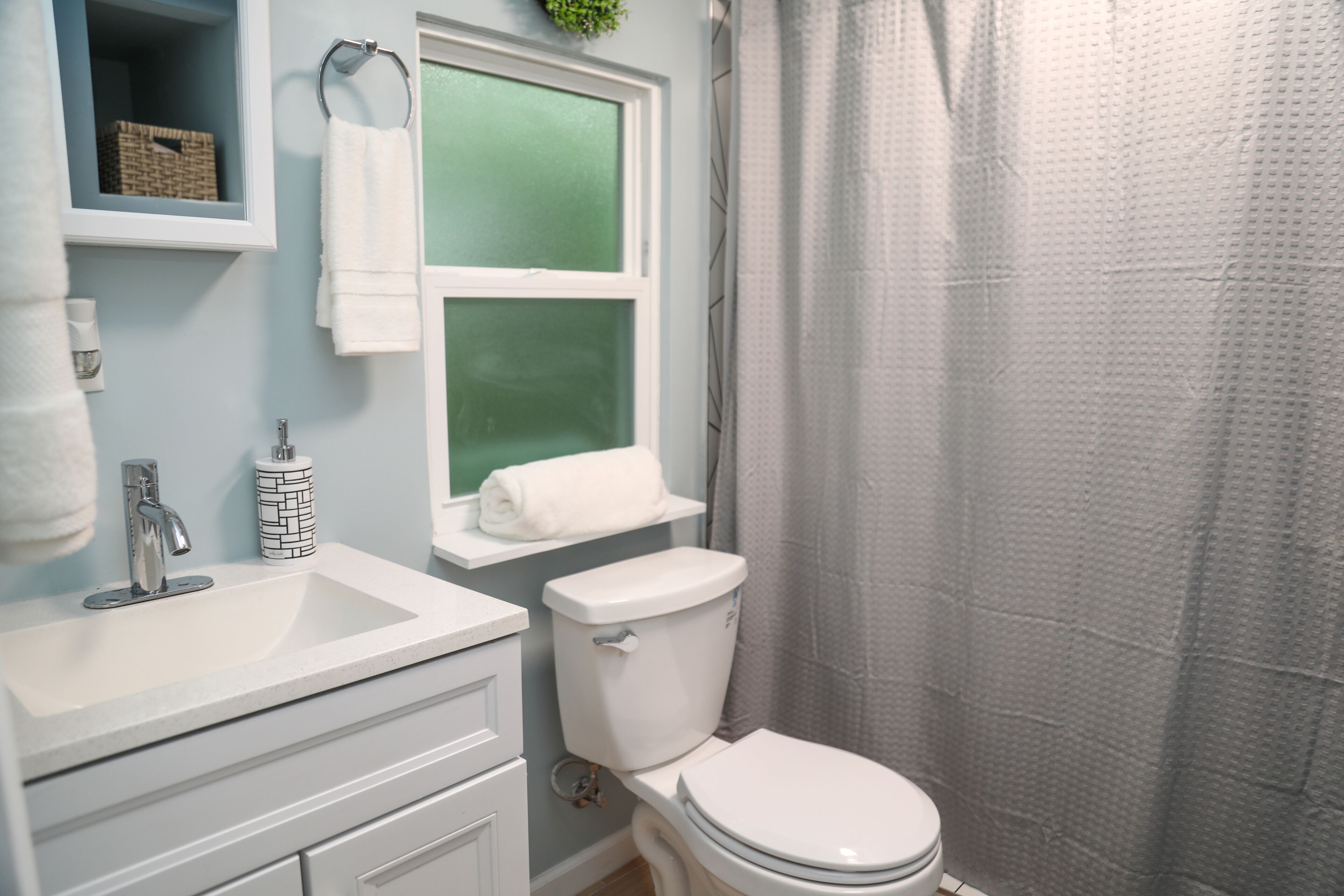 Une salle de bain avec un lavabo blanc, des toilettes et une fenêtre située au-dessus des toilettes.