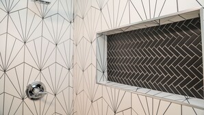 Un baño con un diseño de baldosas geométricas, una ducha con patrón de espiga y un cabezal de ducha visible.