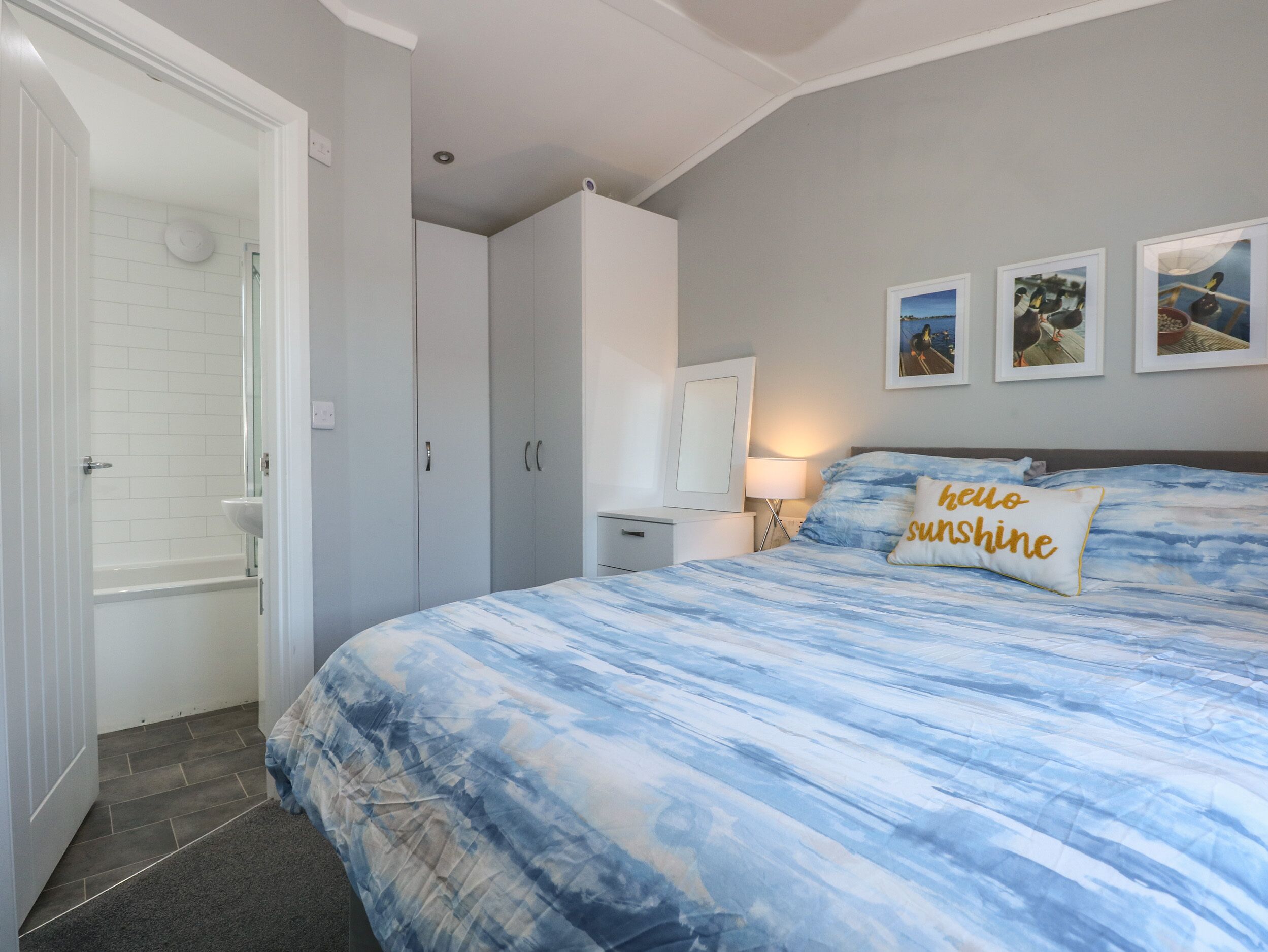 A bedroom with a bed, a nightstand, a dresser, a bathroom with a bathtub, and a door leading to another room.