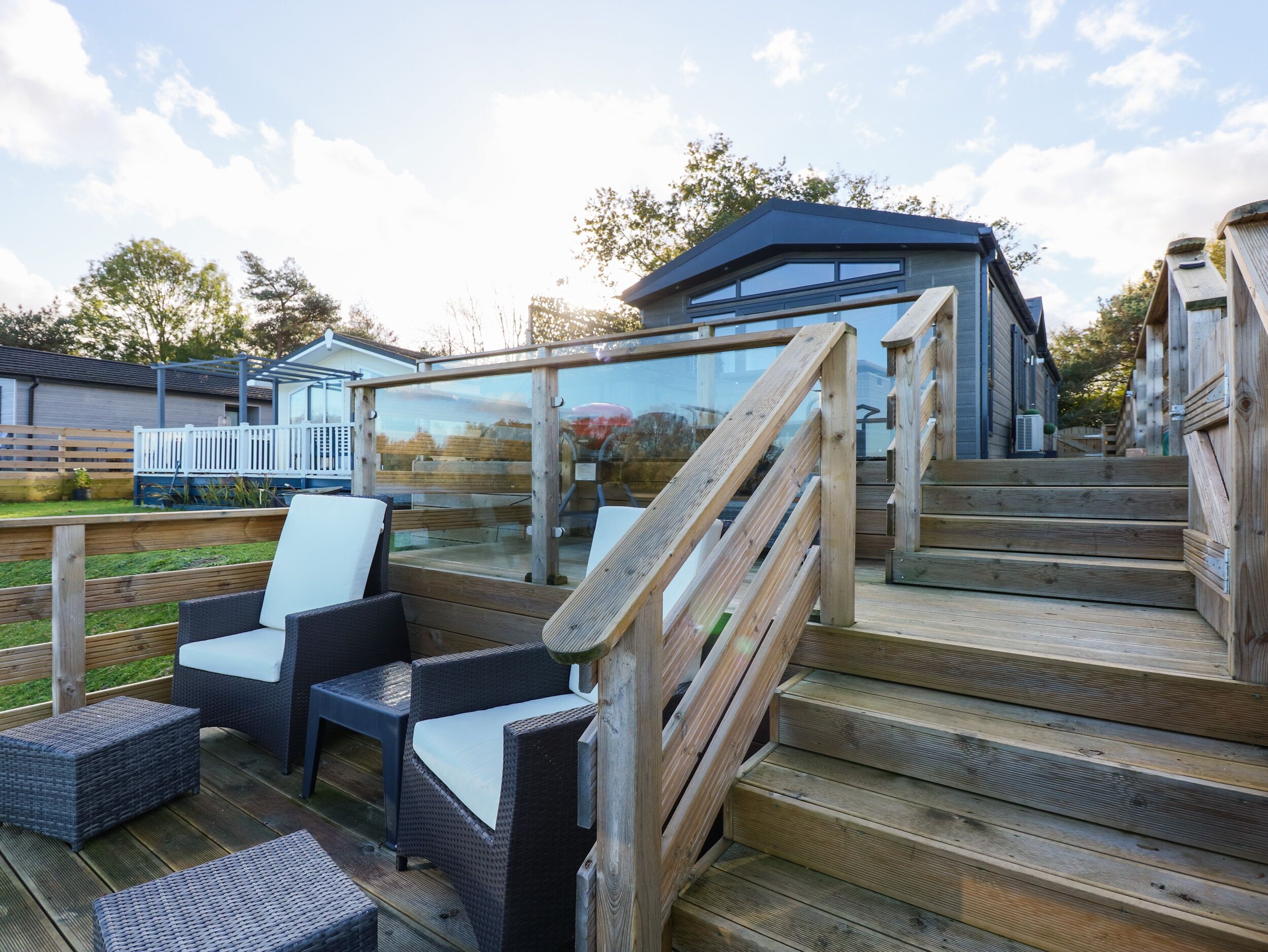 A deck with wicker furniture and wooden steps leading to a glass-enclosed area.
