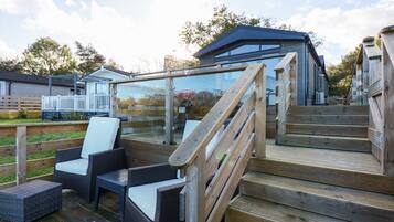 A deck with wicker furniture and wooden steps leading to a glass-enclosed area.