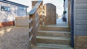 A wooden staircase leading to a wooden deck with a view of a building and a fence. - Lake View Lodge (Bedford)