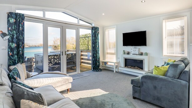 A living room with a sofa, a grey armchair, a fireplace, a television, and a view of the outdoors. - Lake View Lodge (Bedford)