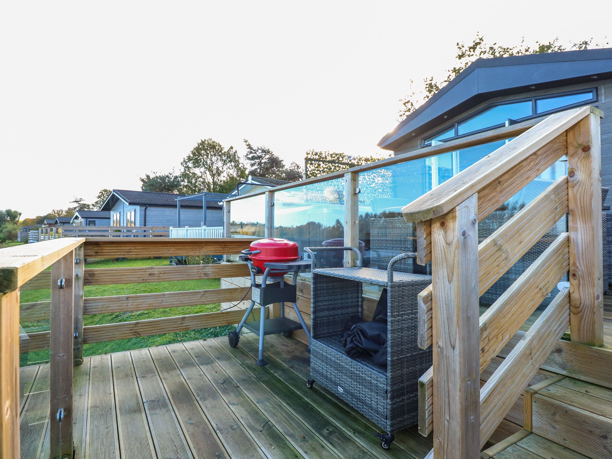 A wooden deck with a barbecue grill, wicker furniture, and a glass-enclosed patio area.