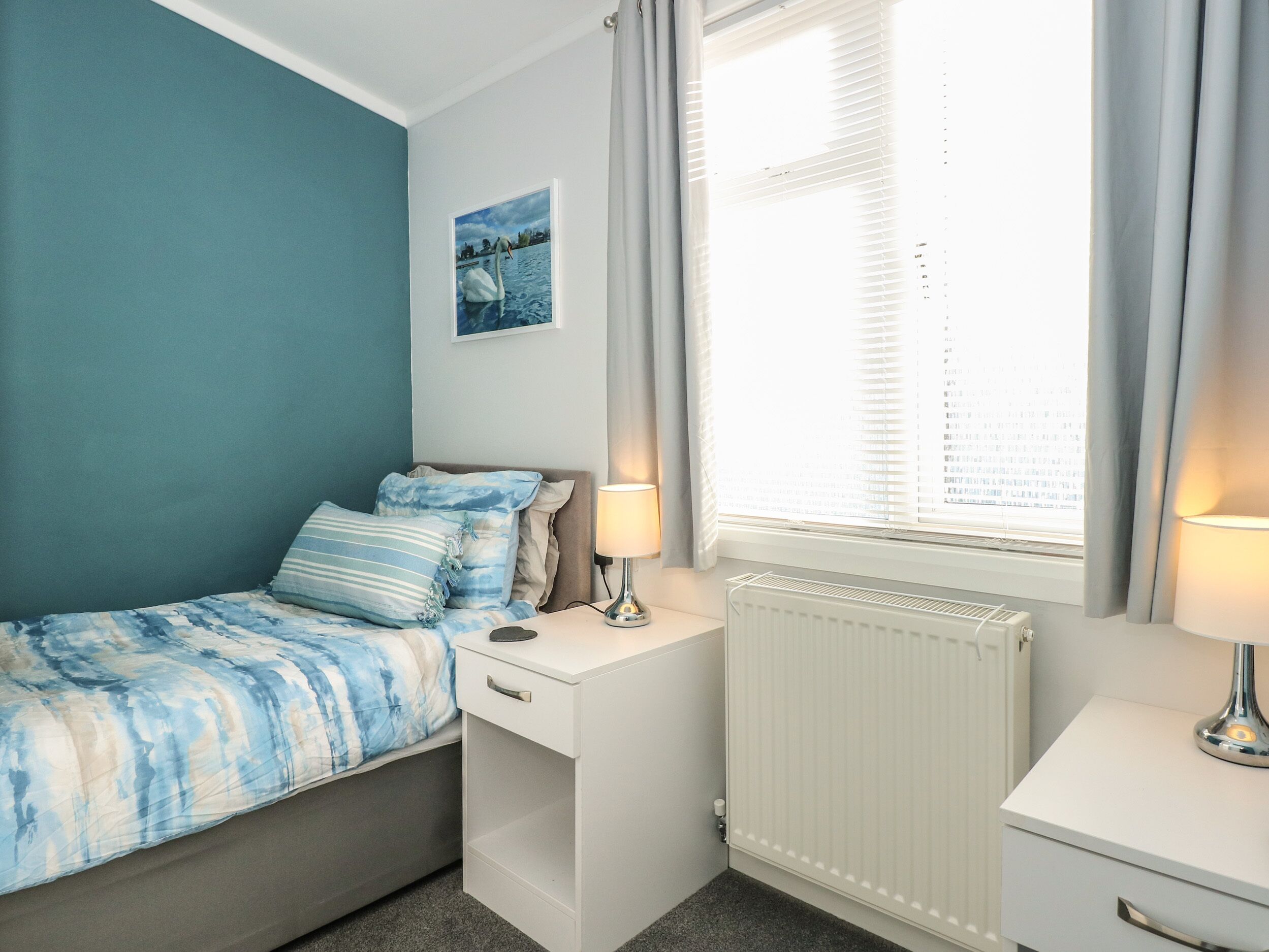 Ein Schlafzimmer mit einem Bett, einem Nachttisch mit Lampe, einem Heizkörper und einem Fenster mit Vorhängen.