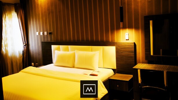 A hotel room with a large bed, a bedside table, a nightstand, and a mirror. - Mo-House Hotels and Apartments (Abuja)