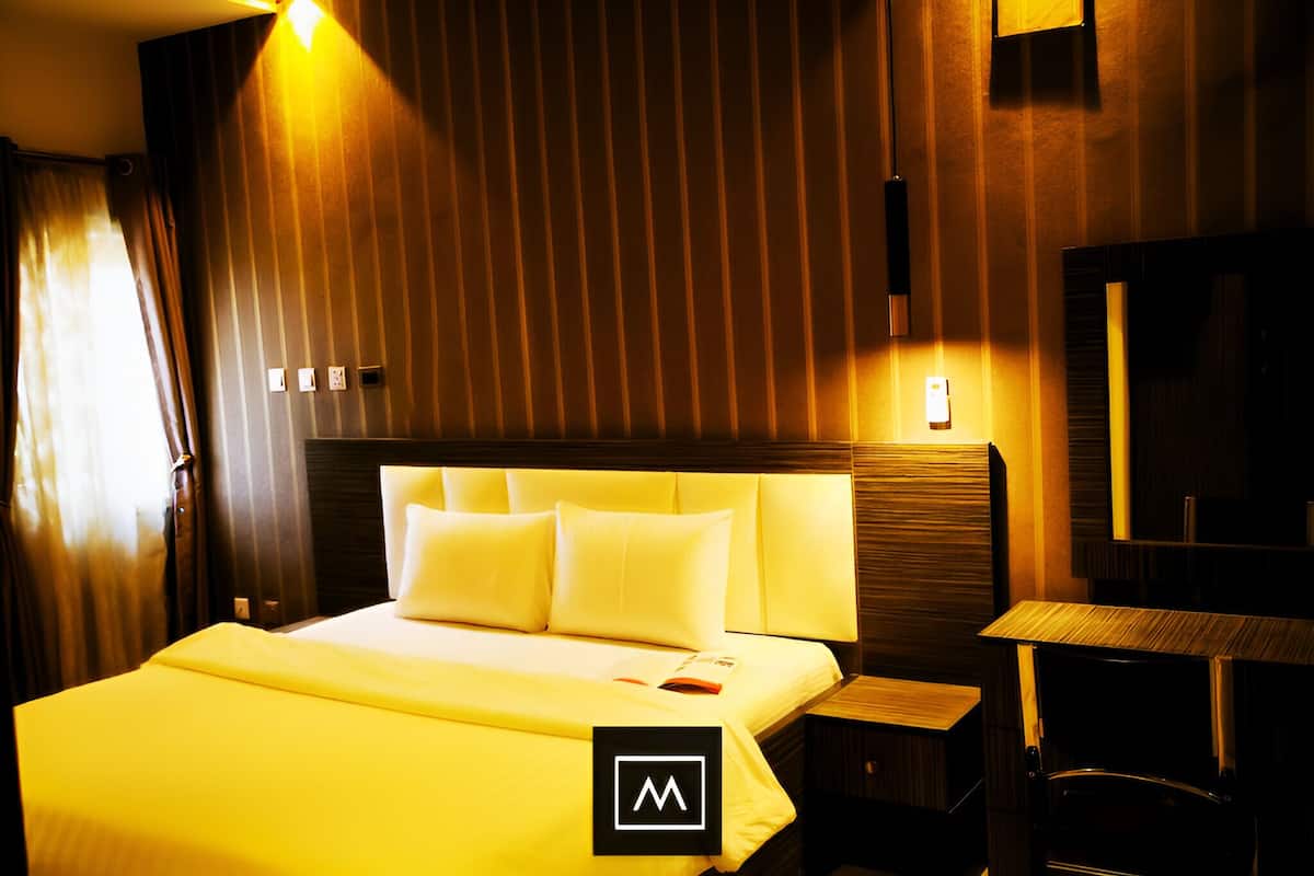 A hotel room with a large bed, a bedside table, a nightstand, and a mirror.