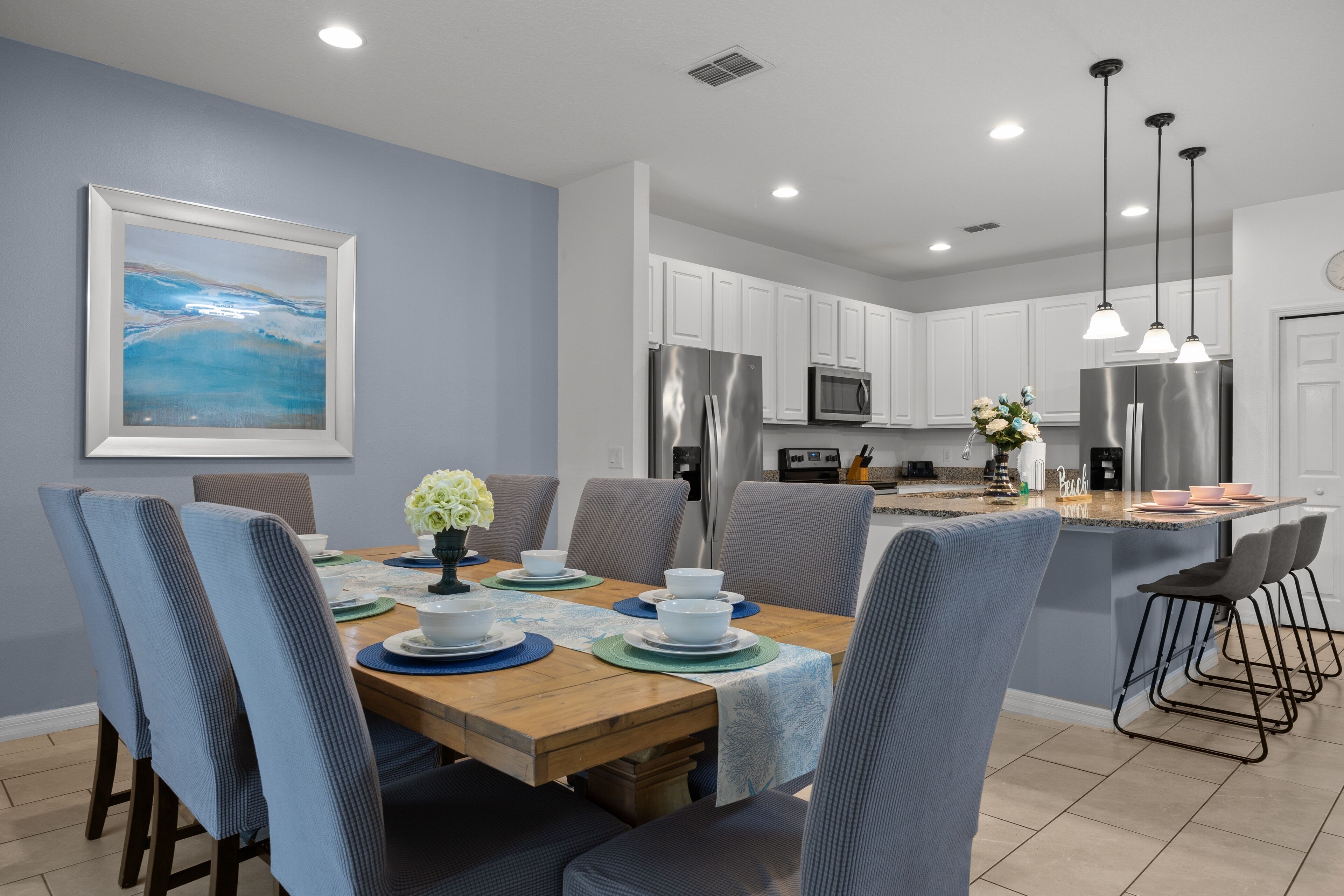 A modern kitchen with white cabinets, stainless steel appliances, and a dining area with a wooden table and blue chairs.