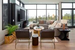 Ein modernes Wohnzimmer mit einem großen Flachbildfernseher, einem grauen Ecksofa, einem Couchtisch und einem Kamin.