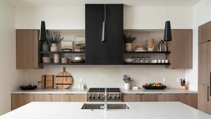 Een moderne keuken met een centraal eiland, houten kastjes en zwarte hanglampen.