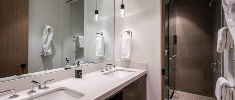 A modern bathroom with two sinks, a large mirror, and a glass-enclosed shower area.