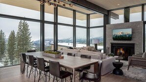 Un salon spacieux avec une grande table à manger, des sièges confortables, une cheminée et une grande fenêtre offrant une vue sur les montagnes.