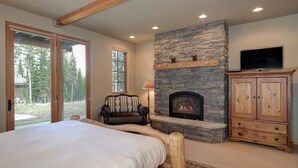 Une chambre avec un grand lit, une cheminée en pierre, un téléviseur et une armoire en bois.