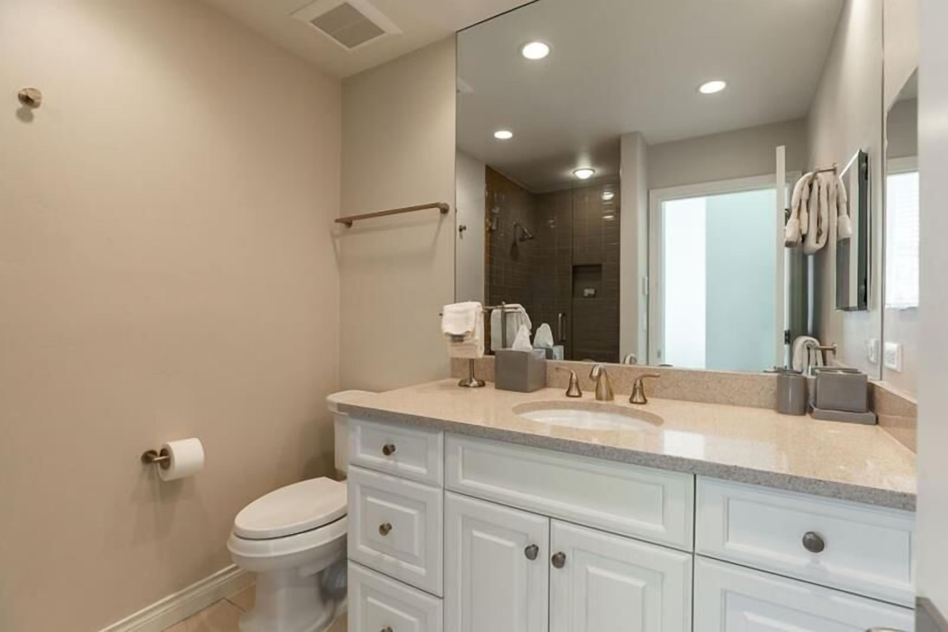 A modern bathroom with a large mirror, a sink, and a toilet.