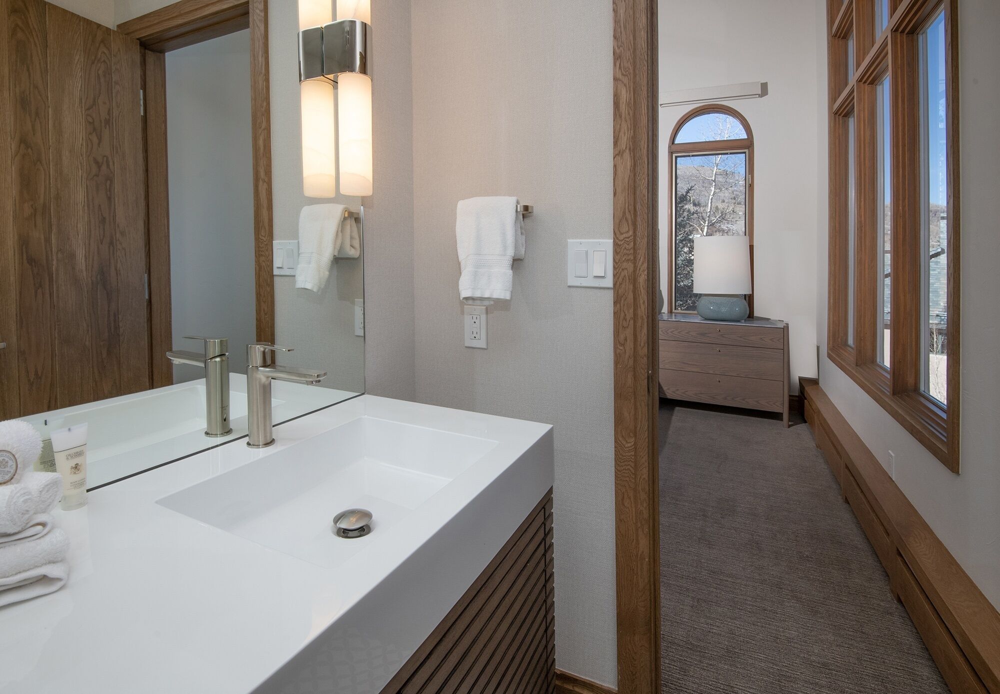 Un baño moderno con un espejo grande, un lavabo blanco y un perchero para toallas.